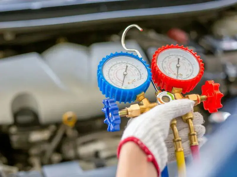Close-up of a gloved hand holding a manifold gauge set used for HVAC system diagnostics