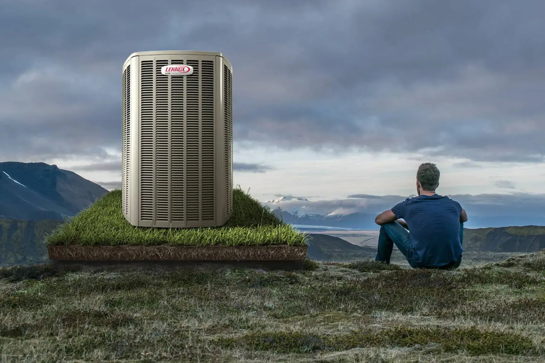 A man sits in nature, contemplating the Lennox air conditioner next to him. The air conditioner sits on a lifted patch of grass and dirt