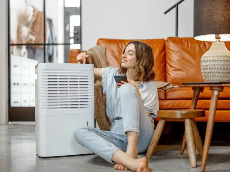 woman happily programming her dehumidifier holding her phone